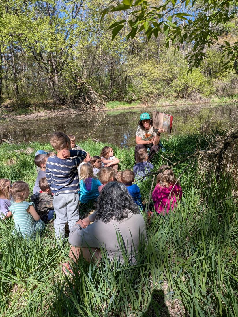 Jenny Peterson reading a picture book to students beside a pond
